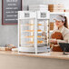 A woman in an apron standing behind a ServIt countertop display case with food.