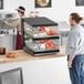 A man standing in front of a ServIt countertop heated display case with food in containers.