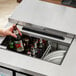 A person using an Avantco stainless steel kegerator to pour a bottle of beer.