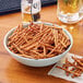 A bowl of Tom Sturgis Thin Stix pretzels next to a glass of beer on a table.