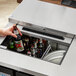 A person using an Avantco stainless steel kegerator to pour a brown bottle of beer.