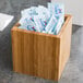 A Cal-Mil bamboo square flatware and condiment organizer on a table in a hotel buffet filled with packets.