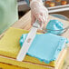 A person using a Choice straight baking / icing spatula to spread blue frosting on a yellow cake.