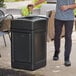 A man throwing a cup into a black Lavex square outdoor trash can.