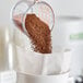 A hand pours brown Toddy cold brew coffee grounds into a white container.