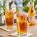 A bottle of Rose's Peach Syrup on a table with a glass of peach iced tea garnished with mint and orange slices. 