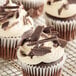 A chocolate cupcake with white frosting and Mona Lisa semi-sweet chocolate shavings.