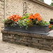A Mayne Fairfield graphite grey window box with orange flowers on a brick wall.