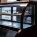 A man using a Turbo Air black refrigerated open display case with food on shelves.