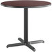 A Lancaster Table & Seating round table with a black metal base and a reversible cherry / black top.