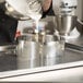 A person pouring white liquid into a silver bowl.