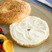 A sesame seed bagel with Daiya vegan cream cheese and fruit on a plate.