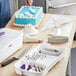 A person using a Wilton cake decorating set to cut a white cake.