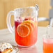 A Carlisle clear polycarbonate beverage pitcher with lemonade, oranges, and cranberries.