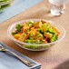 A Carlisle clear pebbled acrylic bowl filled with salad on a table with a fork.
