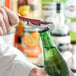 A person using an Acopa waiter's corkscrew to open a green bottle of beer.