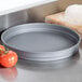 An American Metalcraft hard coat anodized aluminum cake pan on a counter next to pizza dough and tomatoes.