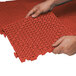 A man's hands interlocking a red Cactus Mat vinyl floor tile.
