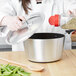 A woman pouring food from a plastic container into a Vollrath Wear-Ever sauce pan.