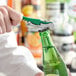 A person using an Acopa Waiter's Corkscrew with a green and silver metal handle to open a green bottle.