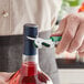 A person using an Acopa waiter's corkscrew with a green and silver metal handle to open a bottle of wine.