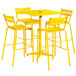 A yellow Lancaster Table & Seating bar table with an umbrella hole and four chairs on an outdoor patio.