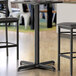 A black Lancaster Table & Seating bar height table base with leveling feet.