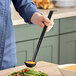 A person using a Cambro black plastic ladle to serve soup from a bowl.