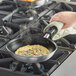 A person using a Vollrath Wear-Ever non-stick fry pan to cook an omelette on a stove.