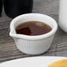 A close up of a white Tuxton fluted ramekin with brown liquid in it.