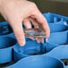 A hand holding a clear glass in a Carlisle blue glass rack extender.