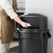 A person putting a black Rubbermaid dome top on a 32 gallon trash can.