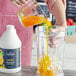 A hand pouring Capora Mango Fruit Smoothie Mix into a blender.