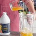 A person pouring Capora Guava Passion Fruit smoothie mix into a blender with orange juice.