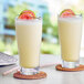 A close up of a glass of Capora Guava Passion Fruit smoothie with fruit on the rim.