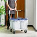 A man using a Vigor aluminum dolly to transport four blue and white plastic buckets.