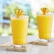 A couple of glasses of yellow liquid with pineapple slices on a table.