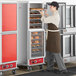 A man in a brown apron taking food out of an Avantco holding cabinet with clear Dutch doors.