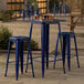 A Lancaster Table & Seating blue metal bar height table and stools on an outdoor patio.