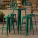 A Lancaster Table & Seating bar height outdoor table with green stools.