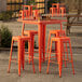 A Lancaster Table & Seating bar table with orange stools on an outdoor patio.