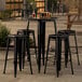 A Lancaster Table & Seating black bar table with four black barstools on an outdoor patio.