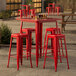 A Lancaster Table & Seating ruby red metal bar table with four backless barstools.