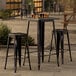 A Lancaster Table & Seating black metal bar table with two black metal barstools.