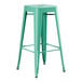 A Lancaster Table & Seating aquamarine metal bar height table with a green metal stool with legs.