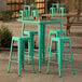 A Lancaster Table & Seating bar height outdoor table with a green finish and four green barstools on a stone patio.