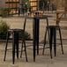 A Lancaster Table & Seating onyx black bar height table with two backless barstools on an outdoor patio.