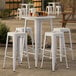 A Lancaster Table & Seating white bar height table with 4 backless barstools on a patio.