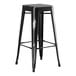 A Lancaster Table & Seating black metal backless bar stool with legs on a bar table.