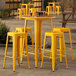 A Lancaster Table & Seating yellow bar height table with yellow stools on an outdoor patio.